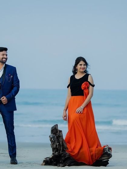 A stylish pre-wedding portrait on the beach. The orange and black gown is a modern and fashionable choice for a non-traditional look.
