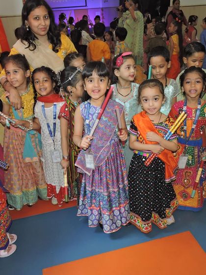 A group of smiling children in colorful Dandiya outfits pose with their dance sticks, ready for the celebration.