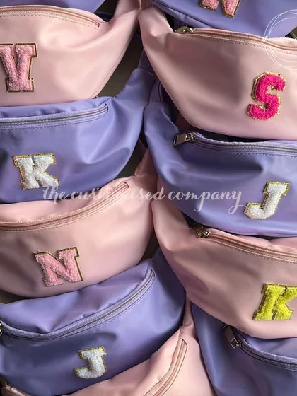 Return favors couldn't get any cuter. These pastel fanny packs in pink and lavender are personalized with colorful chenille initial patches for a fun and trendy gift.