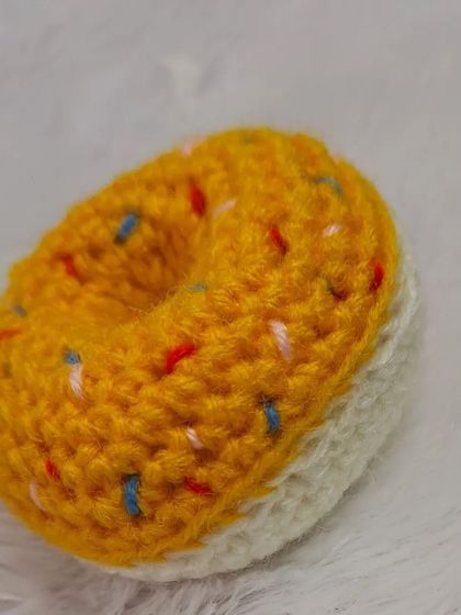 A side view of the crochet donut keychain, showing the two-tone design that looks like a real frosted donut.