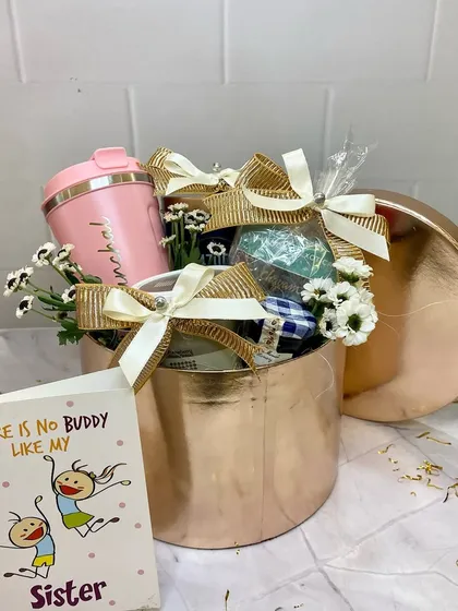 This rose gold hamper for a sister is both chic and personal. It includes a personalized tumbler and other goodies, beautifully arranged in a metallic box with a matching lid.