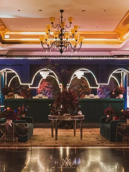 A full view of a contemporary sangeet hall I designed. The decor features a bold, colorful stage backdrop, elegant chandeliers, and unique gold-accented chairs, creating a cohesive and luxurious look.