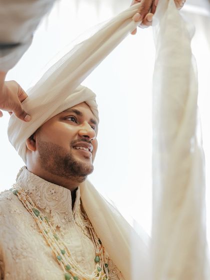 A glimpse into the groom's getting-ready process. The tying of the safa is a significant moment, and his custom Shantanu & Nikhil sherwani with its detailed embroidery is ready for the main event.