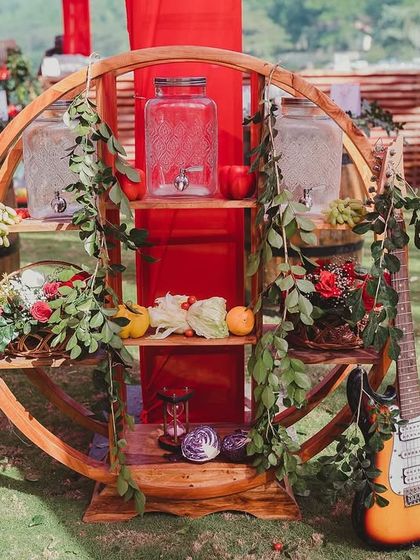 A rustic wooden drink station adorned with greenery, fruits, and an electric guitar, blending a relaxed festival feel with Spanish-inspired details.