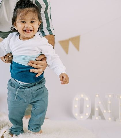 A joyful moment of a one-year-old taking his first steps with a little help. Milestone sessions are perfect for capturing these incredible developmental leaps.