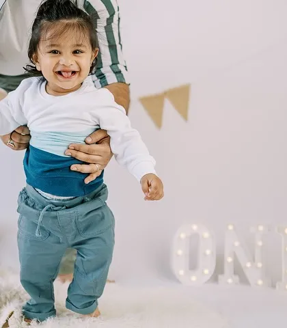 Taking his first steps with a little help. This happy moment is a perfect memory from a first birthday milestone session.