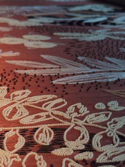 The texture of the embroidered wallpaper comes to life in this detailed shot. The combination of threadwork and beading creates a rich, tactile surface that changes with the light, adding a layer of soft opulence to the space.