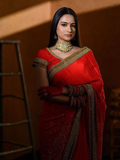 A powerful portrait using shadows and light to create a dramatic effect. The model in a red saree is partially lit, drawing attention to her expression and the texture of the fabric.