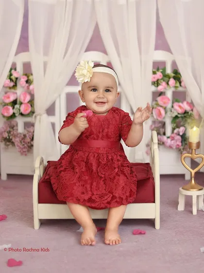 A sweet smile from the toddler in the red dress, surrounded by soft lighting and pink flowers.