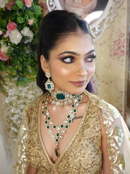 A glamorous look with a golden lehenga and emerald jewellery. The makeup features a dramatic smokey eye and a sleek high ponytail.