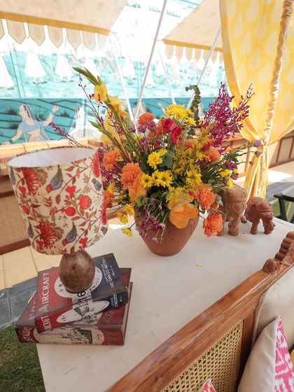 A side table styled with a custom block-printed lampshade, a stack of vintage books, and a terracotta vase filled with flowers, creating a charming and curated corner.