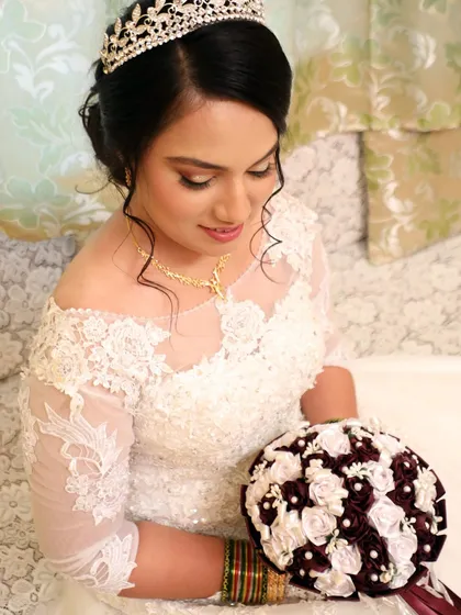 A serene shot of the bride looking down at her bouquet. This angle highlights her elegant updo and the delicate lace details on her gown's sleeves.