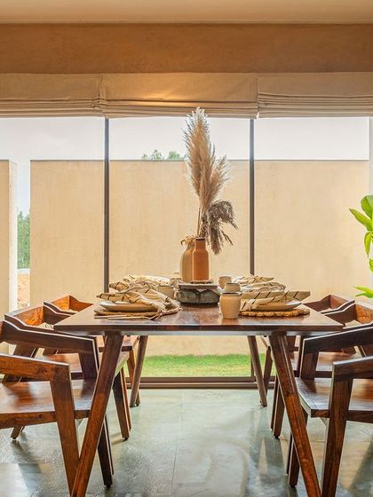 The dining space in the Earth Villa opens directly onto a landscaped deck, blurring the line between inside and out. The floor is finished in green Kota stone, and the solid wood dining set creates a grounded, rustic feel perfect for shared meals.