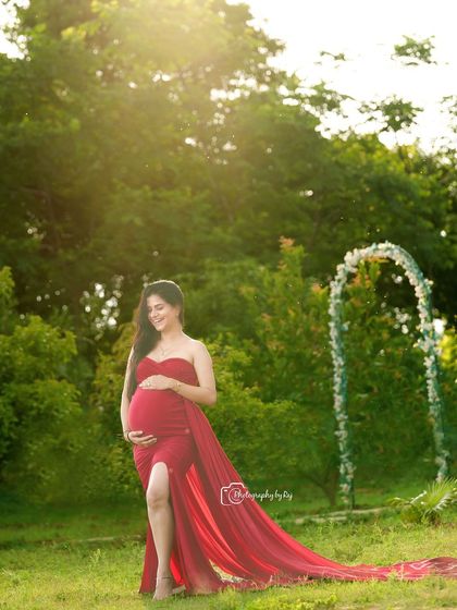A radiant mother-to-be in a red fabric wrap, enjoying a moment of tranquility in our garden. The floral arch in the background adds a beautiful touch.