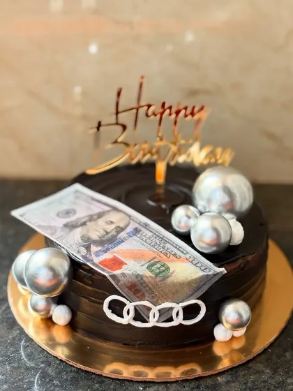 A fun "money" themed cake for a birthday, featuring a rich chocolate truffle base, an edible dollar bill, and silver chocolate spheres.