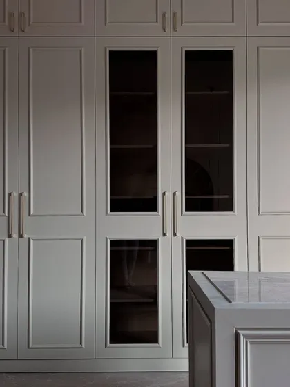 A moody, atmospheric shot of the walk-in closet, focusing on the precise paneling of the wardrobe doors and the sleek marble top of the island.