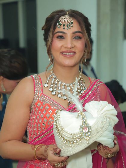 A radiant close-up from my brother's wedding, holding the groom's 'kalgi'. This shot highlights the flawless makeup, the intricate maang tikka, and the stunning polki necklace that completed the look.