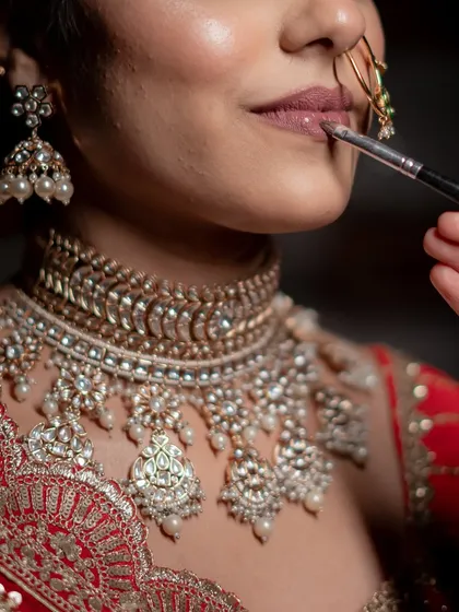 The final touch. This close-up captures the application of a soft nude lipstick, perfectly balancing the intricate jewelry and detailed outfit. It's all in the details.