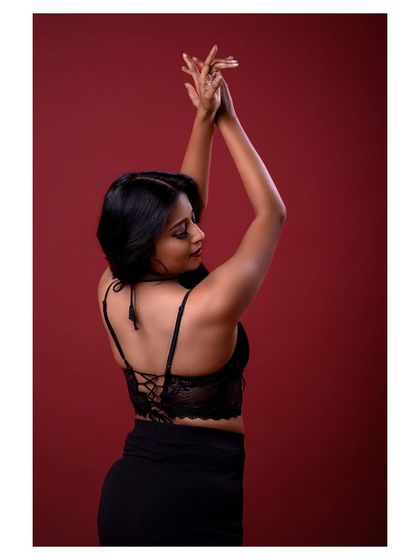 A dramatic and emotive portrait against a deep red background. The model's pose and expression convey a sense of passion and grace.