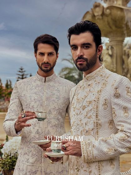 With delicate cups in hand, they embody the spirit of 'Amore'. These two gentlemen wear coordinated but unique ivory sherwanis, showcasing how sophistication can be shared in moments of quiet camaraderie.