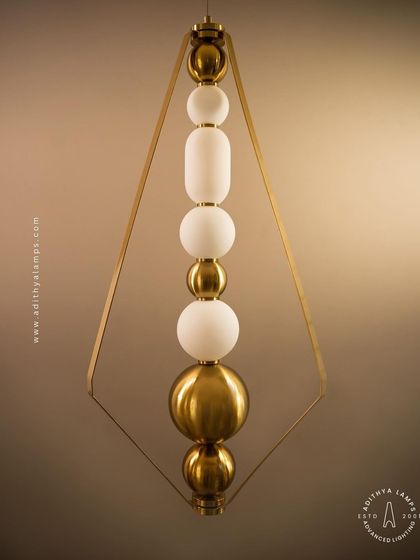 This elegant pendant is framed by a triangular gold structure, enclosing a string of white and gold beads. It's a sophisticated and modern piece that adds a touch of jewelry-like decoration to your space.