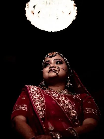 A low-angle shot creating a regal and powerful bridal portrait. The single light source from above illuminates the bride against a dark background, making her the undeniable center of the universe.