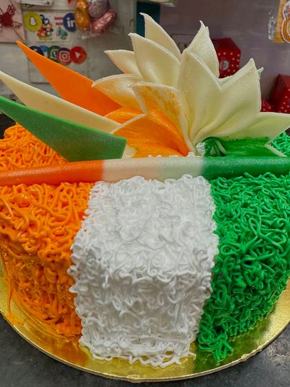 A vibrant Independence Day cake with tricolor frosting that looks like noodles. The design is unique and creative, topped with a white chocolate lotus.