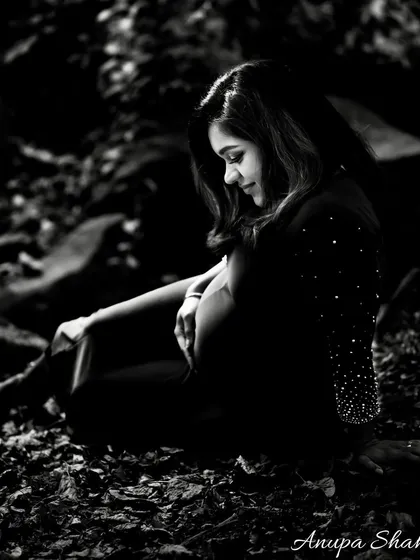 A moody and artistic black and white maternity portrait. The expectant mother is seated in a forest setting, creating a quiet, contemplative, and beautiful image.