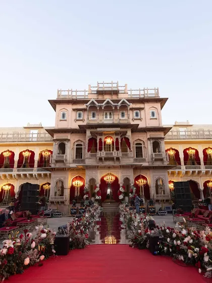 The grand aisle leading to the wedding ceremony at Chomu Palace. A regal red carpet is flanked by lush floral arrangements, setting a majestic tone for the evening.