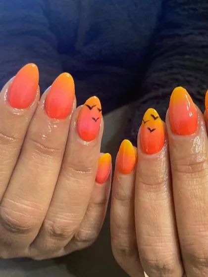 A sunset-inspired ombre manicure. The nails fade from a bright yellow to a warm orange, with tiny birds hand-painted on the accent nails for a beachy vibe.