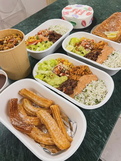 A complete meal order ready for delivery, featuring our churros with chocolate sauce, Mexican rice bowls, and a custom birthday cake. We can handle both the savoury and the sweet.