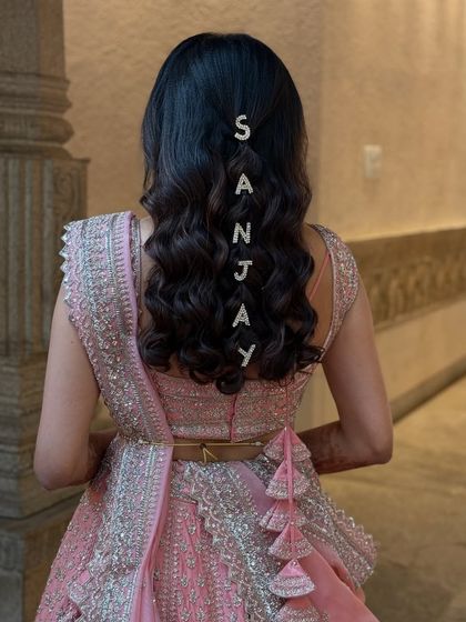 A fun and personalized hairstyle for a Sangeet or reception. The bride's hair is styled in soft waves with crystal letters spelling out the groom's name.
