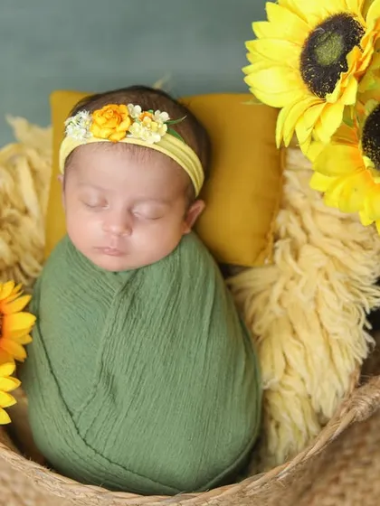 A newborn wrapped in green, nestled in a basket with bright sunflowers.
