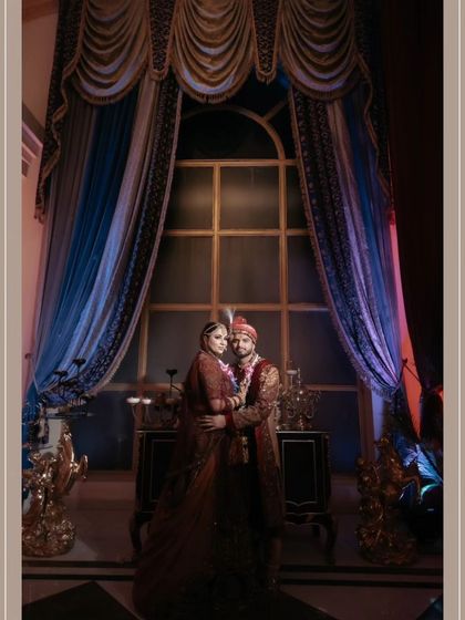 A dramatic, low-light portrait of Akhilesh and Nisha against a grand window with blue curtains, creating a regal and cinematic feel.