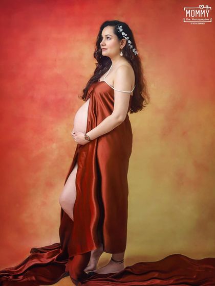 A profile shot that is both powerful and delicate. The slit in the satin drape and the floral hairpiece add a touch of softness to this artistic studio maternity portrait.