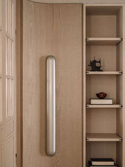 A detail of the custom door handle and shelving in the dining area. The combination of sleek metal and warm wood is a recurring theme, blending raw and refined elements.