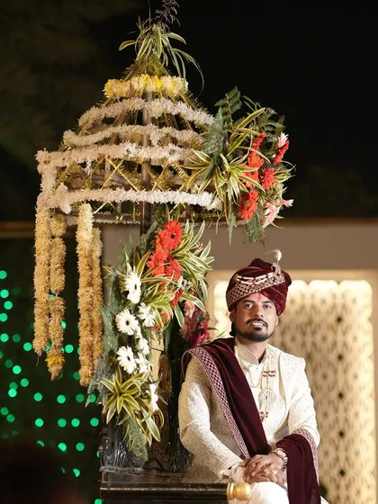 A full-length portrait of the groom, posing with a decorative floral structure at the wedding venue.