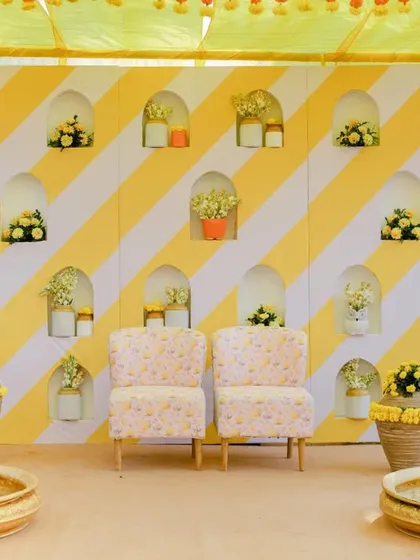The main seating area for the Haldi ceremony, with a yellow and white striped backdrop and elegant floral arrangements.