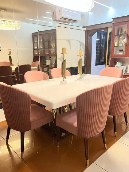 An elegant dining set featuring a white onyx table and chairs upholstered in a pleated pink velvet. The gold-finished table base and chair legs add a touch of warmth and glamour.