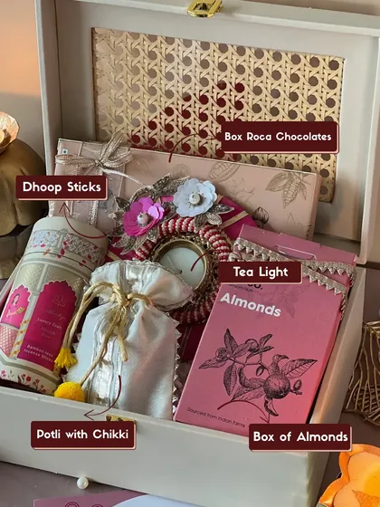 This is my classic 'Gulabi Noor' Diwali hamper, beautifully arranged in a reusable rattan box. It shows exactly what you get, from aromatic dhoop sticks and a decorative tea light to delicious Roca chocolates and chikki-filled potlis.