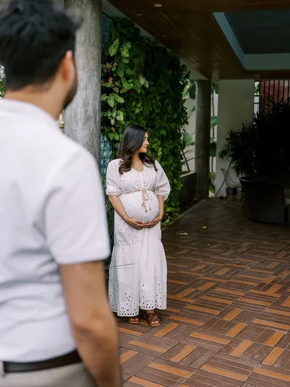 A candid shot of the mother-to-be in a beautiful white dress, framed by her partner in the foreground. This over-the-shoulder perspective creates a personal, story-driven image.