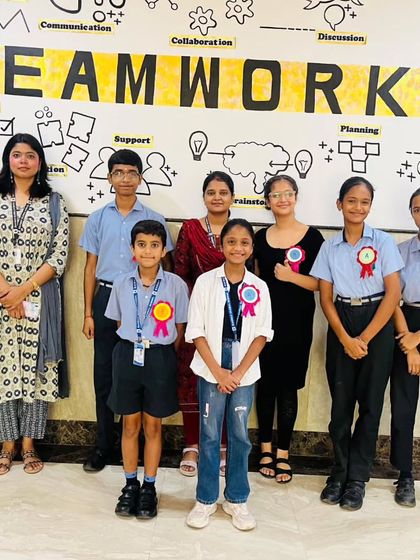A group of students and teachers stands proudly in front of a "Teamwork" mural during the 'Carpe Diem' event. Our literary and arts programs emphasize collaboration and mutual support.