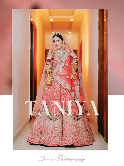 A full-length portrait of the bride in a hallway, looking radiant in her red and pink lehenga.