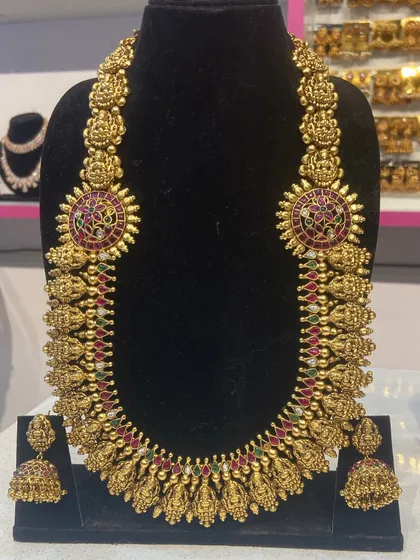 A close up of a grand temple necklace with ruby and emerald-colored stones. The design features goddess Lakshmi motifs, perfect for a traditional ceremony.