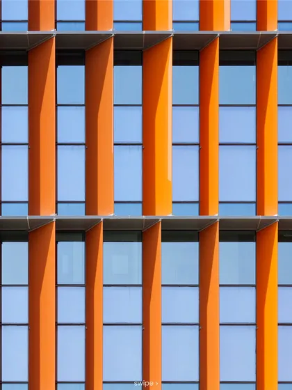 A close-up detail of the orange-hued laminated glass fins on the Infosys Nagpur campus facade. Their primary function is solar shading, with their varying angles optimized to reduce heat gain throughout the day.