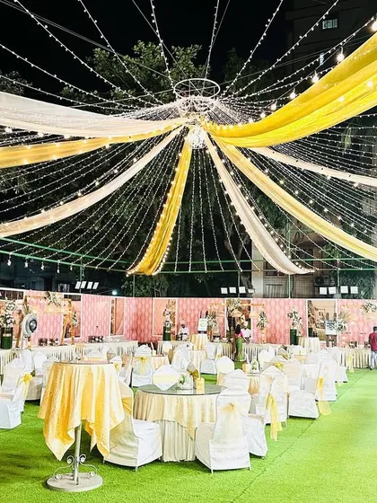 A view of the dining area for an elegant reception. The canopy of white and gold drapes with string lights creates a warm and inviting atmosphere for guests.