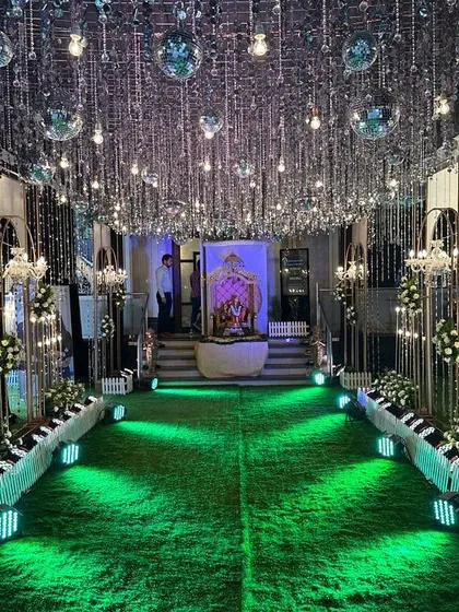 A stunning entrance passage for a Sangeet, featuring a ceiling of cascading crystal strings and disco balls. The green lighting and floral arrangements along the walkway guide guests into the celebration.