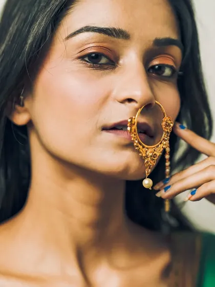 An intense close-up focusing on the model's expressive eyes and the large, ornate traditional nose ring (nath).