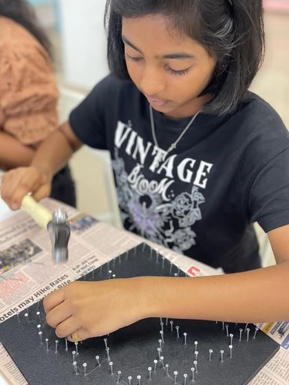 This young artist is hammering nails to create the outline for her flower and butterfly string art design.