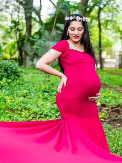 A beautiful solo portrait of an expecting mother in a vibrant pink gown with a long train, looking down at her bump with love.